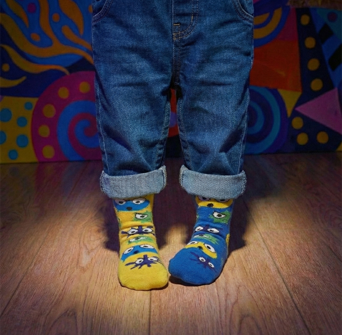 Person wearing blue jeans and colorful socks with a vibrant, abstract-patterned backdrop.